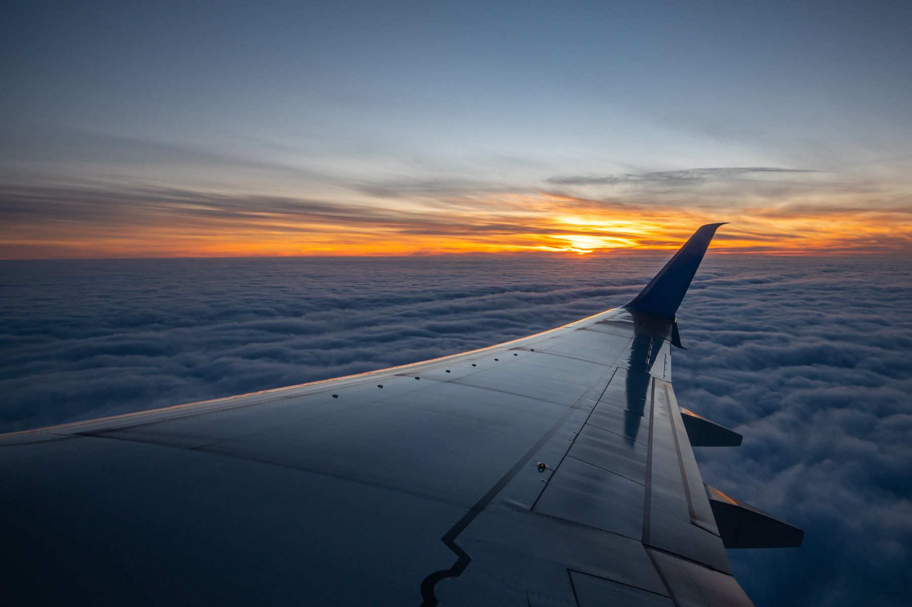 Asa de avião sobre as nuvens ao pôr do sol